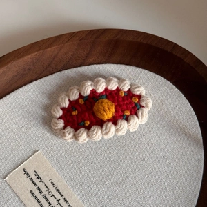 Close-up of a handmade red knitted hair clip with white scalloped edges on a wooden tray