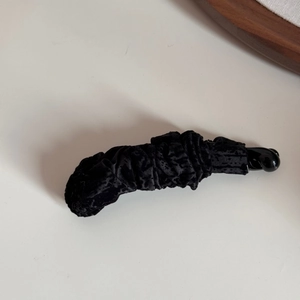 Détail d'une grande pince banane en velours noir avec une texture de tissu froncé élégante