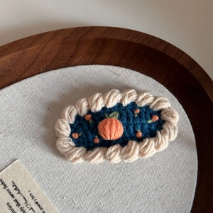 Detailed macro view of a handmade crochet hair clip with orange fruit and blue base