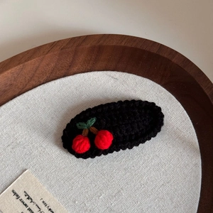 Detail of handcrafted crochet cherry hair clip with red berries and green leaves