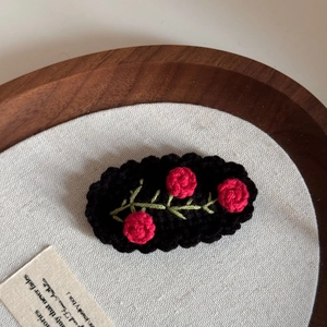 Detail of handmade crochet hair clip with pink roses and green leaves on black knit base