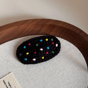 Close-up of a handmade crochet hair clip featuring colorful polka dots on black wool