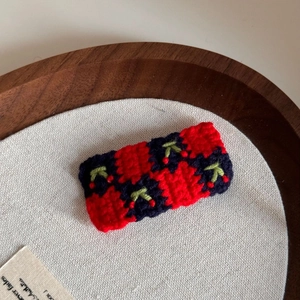 Close-up of handmade crochet hair clip with cherry embroidery and red plaid pattern