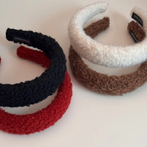 Detail of four fuzzy plush headbands in black, red, beige, and brown with hand-made labels