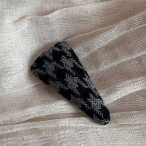 Detail shot of a British style black and grey houndstooth triangle hair clip on linen fabric