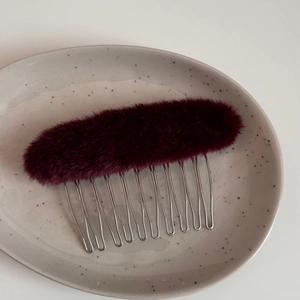 Dettaglio di un pettine per capelli ovale in peluche bordeaux con dieci denti in metallo