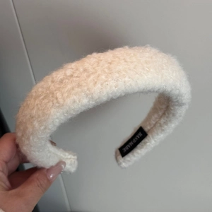 Detailed macro view of white plush faux shearling headband with handmade textile label