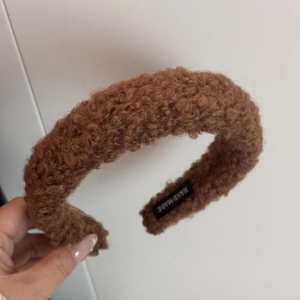 Close-up of brown faux shearling headband featuring a Hand Made woven label