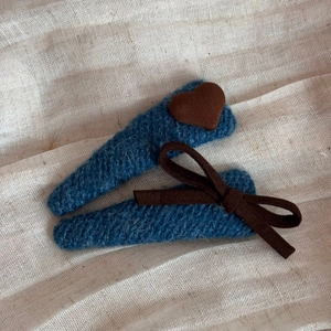 Detail von blau gestrickten BB-Haarspangen mit braunem Herz und Schleife auf Leinenstoff
