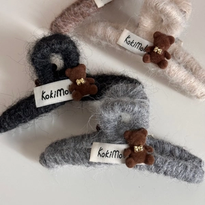 Detail of plush teddy bear hair claw clips in black, beige, and grey colors with fabric labels