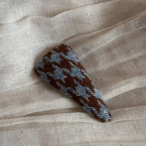 Detailed close-up of a coffee and blue houndstooth knitted triangle hair clip on linen