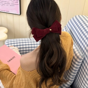 Detail of burgundy velvet bow hair clip with gold metal accent on dark brown curly hair