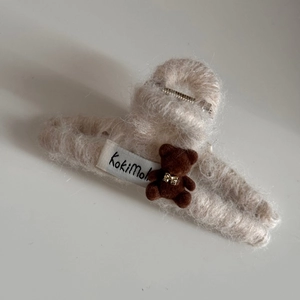 Close-up of beige plush shark hair clip with a cute flocked brown bear and golden bow