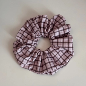 Makroaufnahme von kariertem Stoff-Scrunchie in Rosa und Braun mit feiner Webstruktur