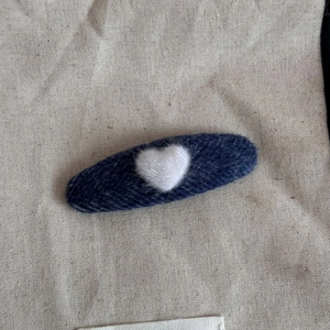 Detail of plush white heart on dark blue wool fabric oval hair clip with burlap texture
