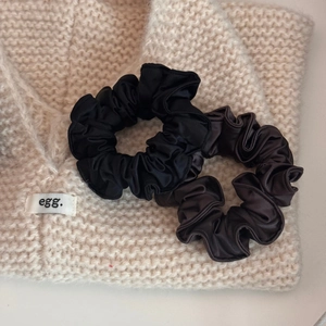 Set of black and coffee satin scrunchies displayed on a warm knitted background texture