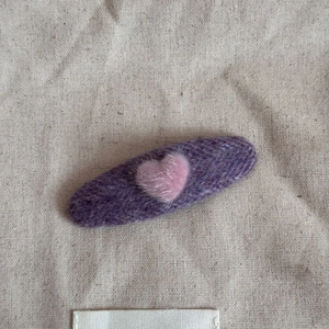 Close-up of purple oval plush hair clip featuring a pink heart on beige canvas background