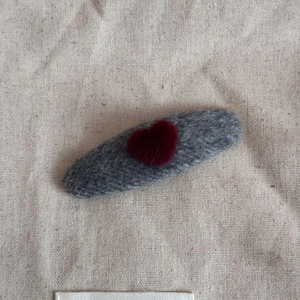 Close-up of a grey knitted oval hair clip with a red heart on beige linen fabric