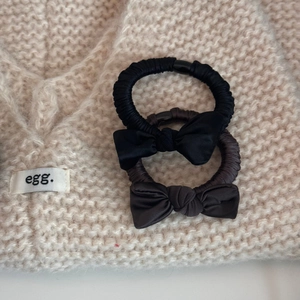 Close-up of black and brown satin bow hair ties on a textured beige knit background