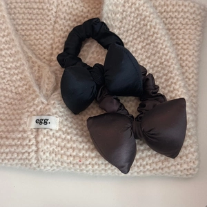 Detailed shot of black and brown satin bow scrunchies on a beige knitted sweater background