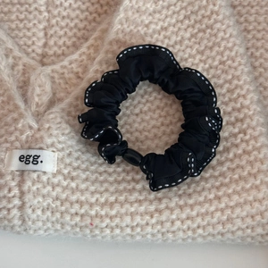 Detail of a black bow scrunchie with white dotted edges on a knitted sweater