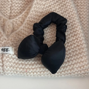 Detailed close-up of a black satin bow scrunchie on a beige knitted background