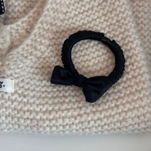 Detailed macro shot of a black satin bow scrunchie on a soft knitted background