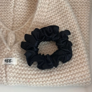 Close-up of black satin scrunchie with silk gloss on soft knit background texture