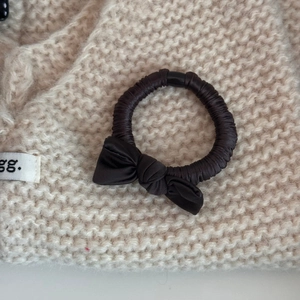 Detail of silk texture bow hair scrunchie in deep coffee on white knit background
