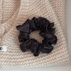 Close-up of silk-like dark brown scrunchie with soft pleated texture on knit fabric