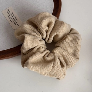 Close-up of a light coffee knitted scrunchie with textured fabric on a wooden tray