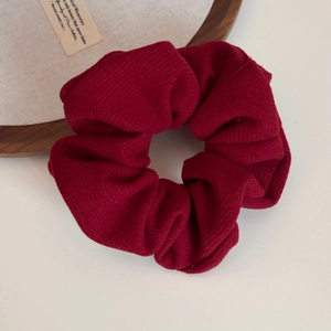 Close-up of burgundy fabric scrunchie with soft pleated texture on vintage wooden tray