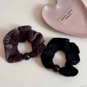 Brown and black plush scrunchies with decorative beads on a minimalist pink heart tray