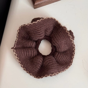 Dettaglio dell'elastico in maglia marrone scuro con bordi dorati e texture in lana
