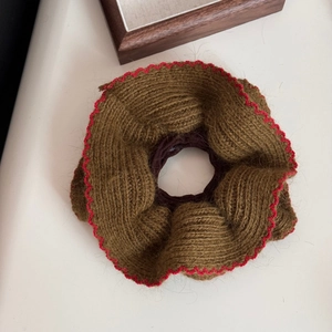 Dettaglio di un elastico per capelli in maglia con bordi smerlati rossi e trama in lana