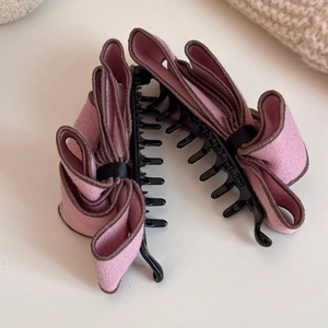 Detailed view of large pink suede bow banana clips with brown stitching on a beige surface