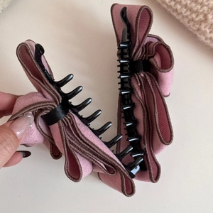 Detail of pink faux suede bow hair clip with brown scalloped edges and black grip