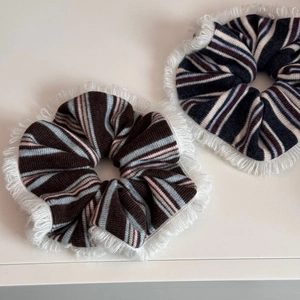 Close-up of two knitted stripe hair scrunchies featuring soft white fringe edges