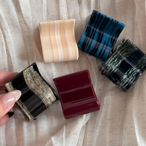 Detail showing five assorted acetate hair claws in various patterns on a soft fabric
