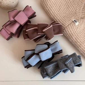 Close-up of four suede bow banana clips in pink, brown, blue, and grey with contrast stitching