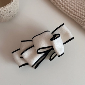 Detail of a beige multi-layer bow banana clip with black edges in soft faux suede fabric