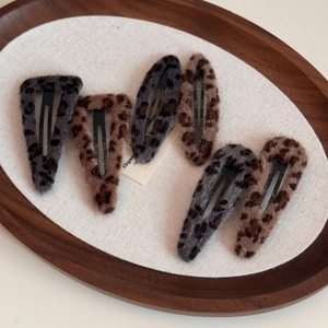 Close-up of leopard print plush BB hair clips in grey and brown on a wooden tray