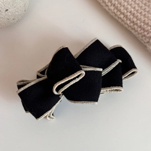 Detailed close-up of a black faux suede bow banana clip with elegant white stitching accents