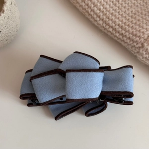 Close-up of light blue suede banana clip with layered bow and dark brown fabric trim