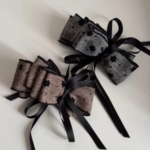 Detail of tweed bow hair clip with black floral patterns and long satin ribbons