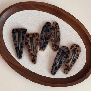 Close-up of leopard print plush hair clips in brown and grey tones on a wooden tray