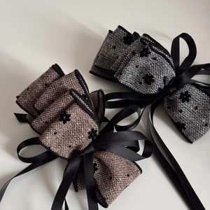 Detail of tweed bow hair clips with floral embroidery and long black satin ribbons
