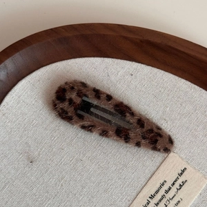 Close-up of leopard print plush snap hair clip on a minimalist canvas and wooden background