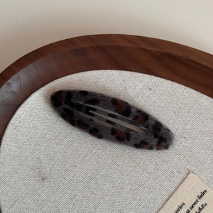Detailed view of a leopard print plush BB hair clip on a rustic wooden tray and linen cloth