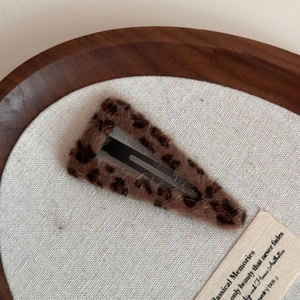Close-up of a triangular leopard print plush hair clip with faux fur texture on wood